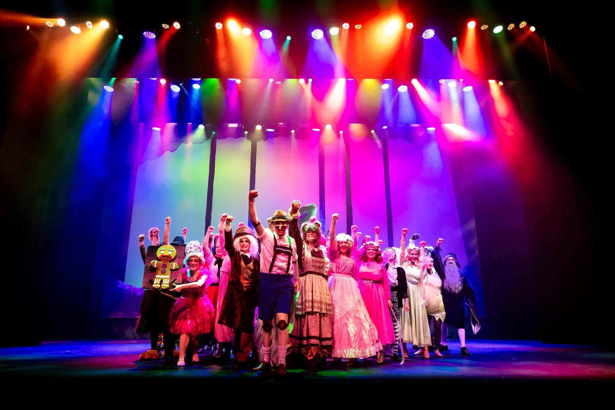 The full Shrek company in costume — fairytale creatures, wigs and gowns under rainbow lights